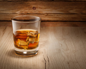 A glass of whiskey with ice cubes is on the table. Space for text
