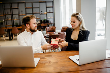 A bearded man Manager sits at the office Desk and gives a gift to his beautiful colleague at work