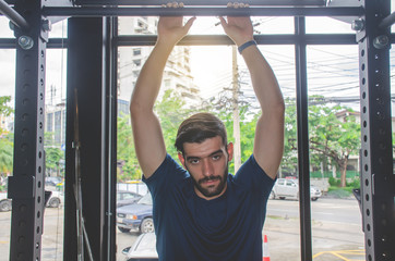 Fototapeta premium fitness, sport, training and lifestyle concept - Portrait of handsome strong athletic man exercising on horizontal bar in fitness gym and looking at camera.