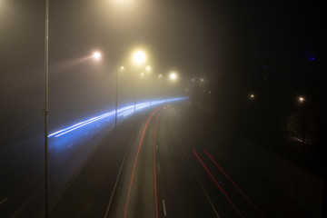 A traffic scene in a foggy night with blurry street lights and motion tracks of car lights