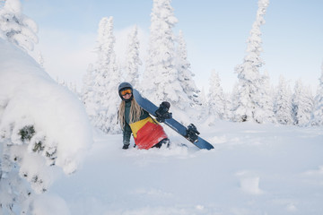 Woman snowboarder wearing long dreadlocks and ratsa hoody in white winter forest walking in snow powder