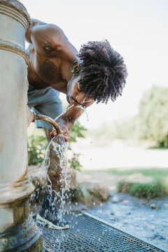 Young man during workout, drinking from fountain in a park