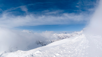 The road during the start of a snow blizzard on top of a mountain with a beautiful view on a sunny day