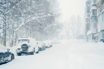 Heavy snowfall. Snow-covered cars parked near houses in winter city