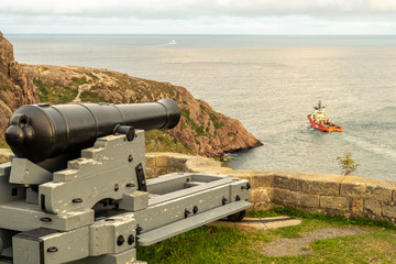 A modern deep water drilling rig support ship going out to sea under the watchful old cannon from the Queen's Battery #4, St. John's, Newfoundland