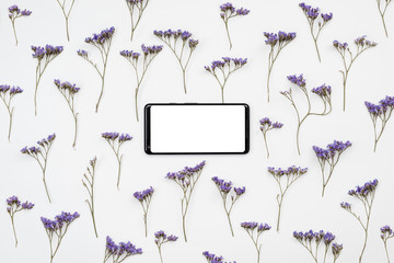 On a white background there are wildflowers and a smartphone with a blank screen. Place for text,