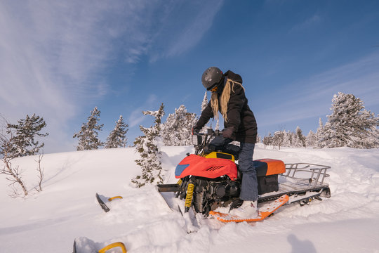 Beautiful woman driving snowmobile in deep snow winter forest on mountain top with amazing landscape view