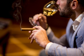 Young man tasting white wine and smoking cigar