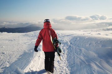 Woman snowboarder holding snowboard walking on mountain top, preparing to snowboarding