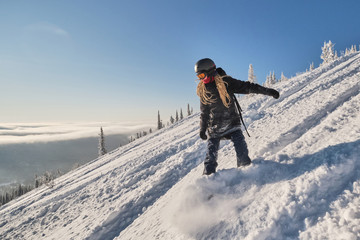 Female snowboarder wearing hoodie riding on mountain slop in big snow powder. Sunny winter day in...