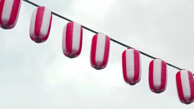 Oriental paper red-white lanterns Chochin hanging on gloomy cloudy sky background. Japanese lanterns hanging on sky background.