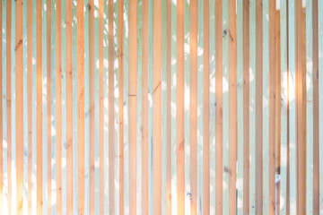 Wood battens in the vertical postion settle on the wall for fence and hording outside of building. It's a background of light from leaf of tree shadow to battens.