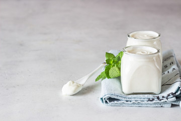 Two portions of natural homemade organic yogurt in glass jars with mint on a grey slate background. Fresh and natural fermented milk product.