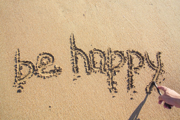 Hand paints word Be HAPPY on the sand by wooden stick.