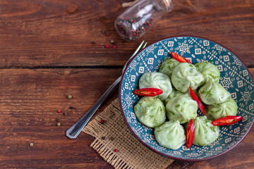 Boiled khinkali made of dough with spinach. Garnished with Red Chilli, Dill and Parsley. On a wooden background.