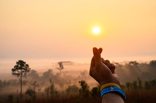 The woman's hand uses a finger to mark a small heart under the sunrise at Thung Salaeng Luang.