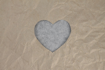 Fototapeta premium Gray felt heart on craft paper. Crumpled paper texture. Valentine's day stock photo for web, print and wallpaper. With empty space for text.