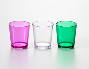 A set of three drinking glass of different colours, purple, white and green. Isolated on a white background.