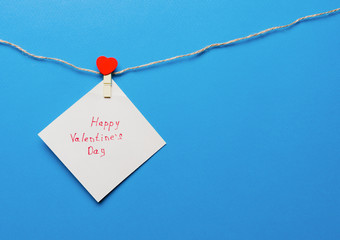 Valentine's day greeting written on note paper, secured on a rope with a clothespin with a red heart on a blue background