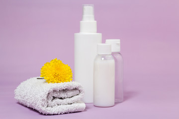 Cosmetics for body care after bathroom. White cotton fluffy towel with yellow flower on it. Bottles and jars with cream and shampoo.