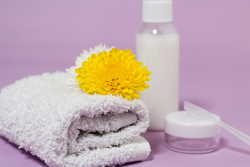 Fototapeta na wymiar Cosmetics for body care after bathroom. White cotton fluffy towel with yellow flower on it. Bottles and jars with cream and shampoo.