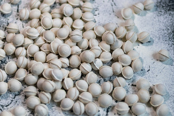 Flour pours onto the table. In order to make dough products, mini-dumplings are not stuck. Dumplings fall into flour. Dark marbled background.