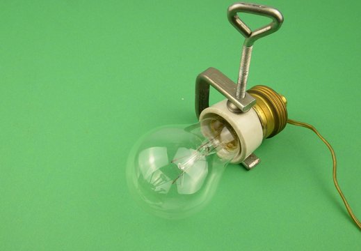 Risparmio energetico, riduciamo lo spreco di energia elettrica: vecchia lampadina e relativo portalampada in ceramica bianca con filo bloccata da da una morsa d'acciaio