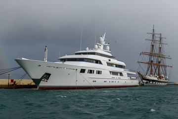 White luxury super yacht and sailing ship moored in marina.