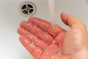 Fototapeta premium Mann hält seine Hand unter laufenden Wasserhahn