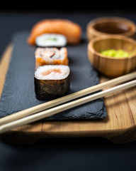 View of sushi rolls, maki, uramaki, nigiri and sashimi set served on stone slate.