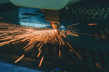 Machine for laser cutting of metal. Laser head cuts the sheet with a beam, sparks scatter in...