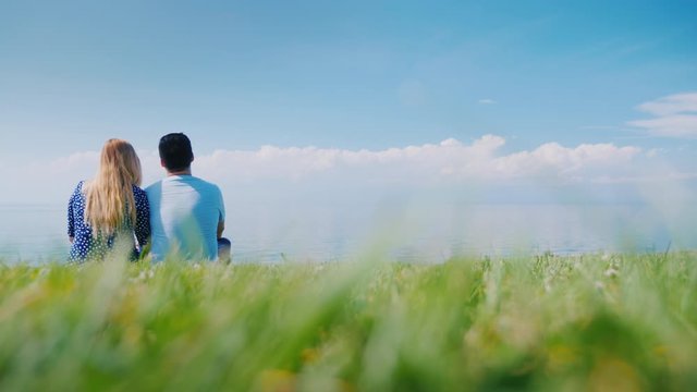 Rear view of A young couple is sitting on a green lawn in a picturesque place near the lake