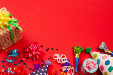Festive golden and purple stars of confetti  and a present, birthday caps on a red background.