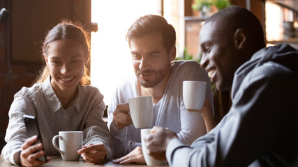 Happy diverse friends have fun watching video in cafe