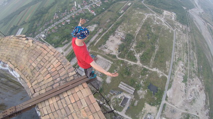 Man without any safety equipment walking on a thin rusted rail on top of a high abandoned stack...