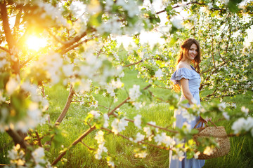 Girl with a basket in her hands stands at sunset in a flowering garden
