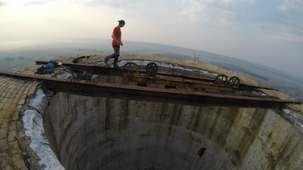 Man without any safety equipment walking on a thin rusted rail on top of a high abandoned stack...