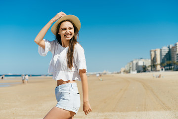 young girl in summer clothes walks along the beach sand and squinting from the sun looks over her shoulder over the sky