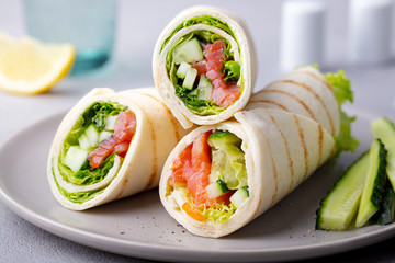 Wrap sandwich, roll with fish salmon and vegetables. Grey background. Close up.