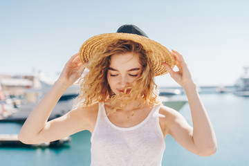 Fototapeta na wymiar cute girl modestly dropping her eyes holds a hat on her head from the sea breeze