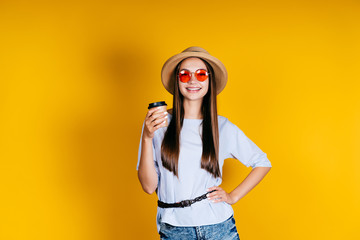 the girl in the hat disassembles a cup of coffee in her hand, smiling boldly akimbo
