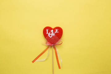 Fototapeta premium Closeup of a heart with a decor on a stick on a yellow isolated background. Spell love in white letters.