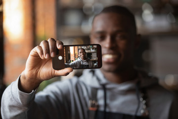 Positive black waiter making selfie on cellphone in restaurant