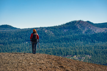 A hiker crests a ridgeline with a view of forested mountains