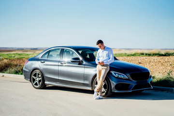 Young businessman leaning against car on country road using smartphone