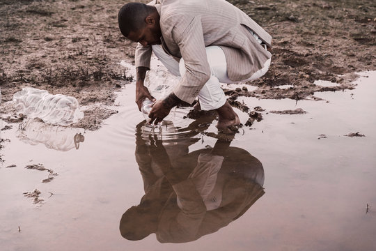 Young man filling plastic bottle with water at a water hole