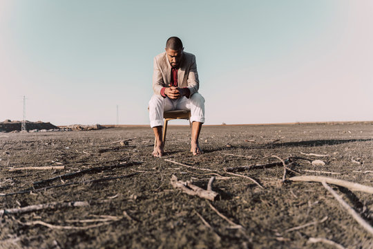 Pensive young man sitting on chair in barren land