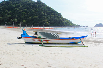 A traditional boat that is leaning on a white sand beach. Green hills and bays in the background.