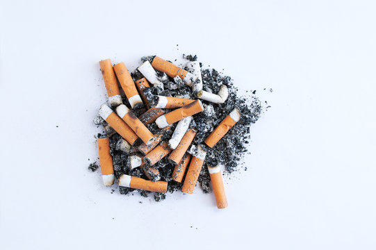 Cigarette butts with a yellow filter near a pile of ash on a white background.
