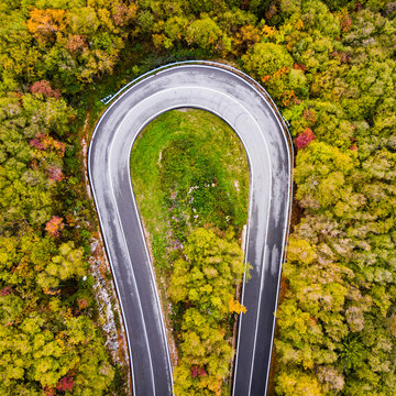 Italy, Trentino, Trento, Aerial view of curve of empty highway stretching across autumn forest in European Alps